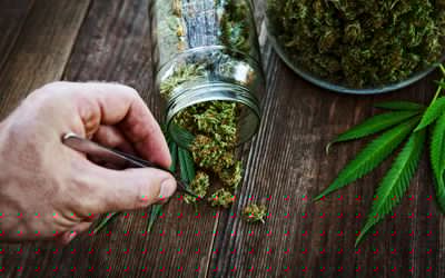 Cannabis bud pouring out of a glass jar on wood background