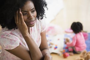 Frustrated mother rubbing her temples while child plays in background