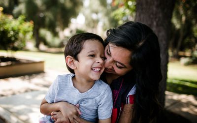 妈妈在一个公园拿着她微笑的儿子在一个晴天。