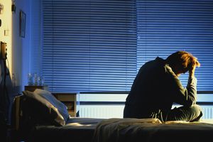 愁眉苦脸的男人坐在医院的床上，头在手里，晚上