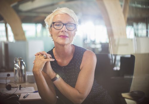 Confident mature woman leaning on her desk in a modern office