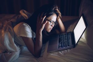 Distressed young woman looking at laptop in bed in the dark