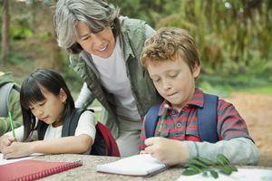 学生们在野餐桌上做笔记，一个成年妇女在旁边看着