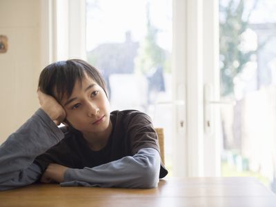 一个男孩坐在桌子旁，头握在手里