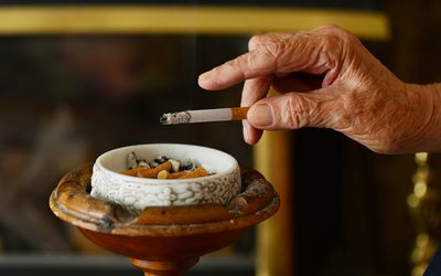 关闭一个皱纹的，老年的手敲打灰烬到烟灰缸里