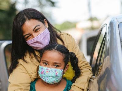 站立在汽车附近的拉丁克妈妈和女儿。