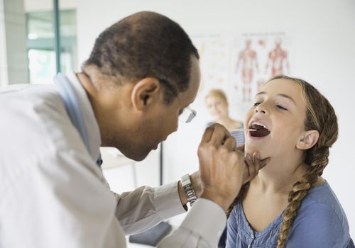 Doctor examining girl with tongue depressor in clinic