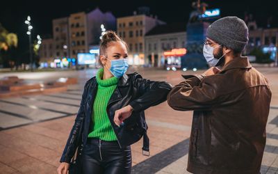 两名成年人戴着面具和触摸肘部互相问候