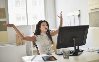 一个愤怒的女人坐在她的办公桌前，两手朝天