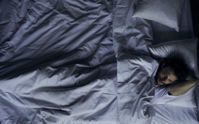 一张照片上，一个男人醒着躺在皱巴巴的床上。