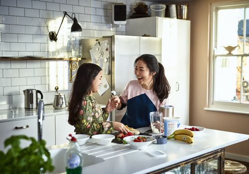 女人拿着用勺子盛着的酸奶对着女孩，笑着，威胁要把食物涂到女儿的脸上，胡闹，玩，联络感情