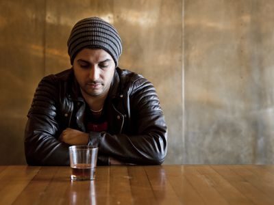 神情沮丧的男子端着一杯酒坐在桌旁