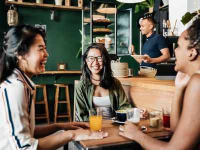 Three young friends sitting down in their favorite coffee shop, laughing and catching up with each other.