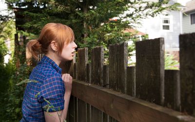 女人越过篱笆窥视邻居家的院子。