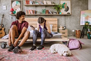 坐在公寓的床上的年轻多种族夫妇在公寓，准备跑步，坐在他们附近的蓬松狗