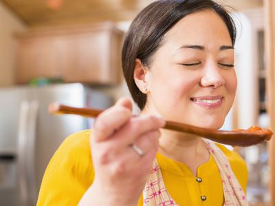 Woman tasting sauce from a wooden spoon