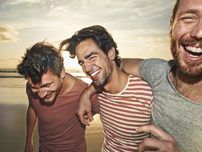 三个男性朋友在海滩上，微笑的照片