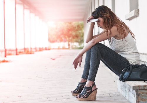 Woman sitting on step with phone in hand looking exhausted or sad