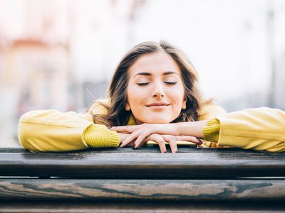 Woman leaning against a railing with her eyes closed and smiling