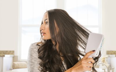 Woman brushing long dark, wavy hair with a large, flat hairbrush
