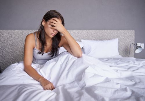 woman holding head in bed