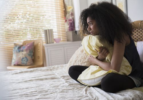 USA, New Jersey, Teenage girl (14-15) sitting on bed, embracing pillow