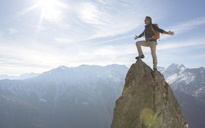 Hiker stands on pinnacle summit, arms outstretched