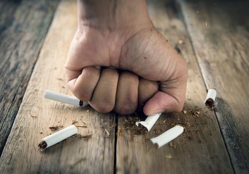 Cropped Hand Of Man Hitting Cigarette On Wooden Table