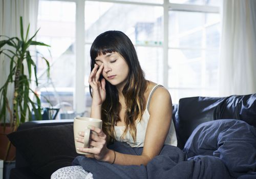 闭着眼睛摸她的脸，手坐在沙发上用一杯咖啡的女人