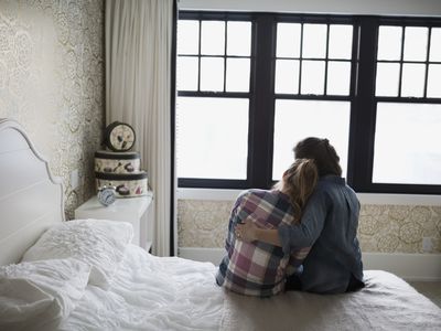 Mother embracing daughter sitting on bed