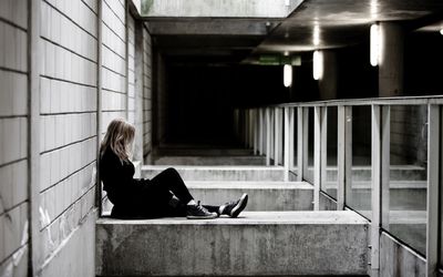 A depressed young woman sits alone against a concrete pillar. Denmark
