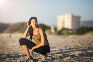Tired young female athlete crouching at beach