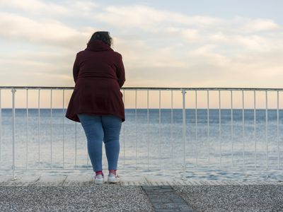 一个穿红色夹克的女人站在栅栏前眺望大海