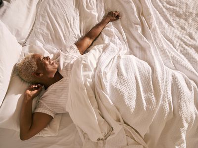 一名短的灰色头发，躺在床上伸展，微笑着。