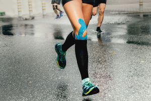 Woman runs in rain with blue kinesiology tape applied to knee