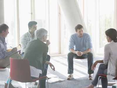 一群男人和女人坐在一圈椅子上谈话