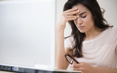 Stressed woman rubbing her forehead at laptop