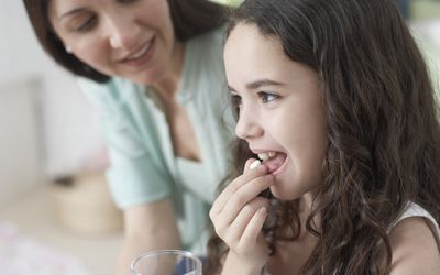 Woman helping young girl take medicine in bedroom