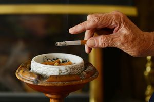 特写镜头：一只布满皱纹的老手在烟灰缸里敲打着烟灰