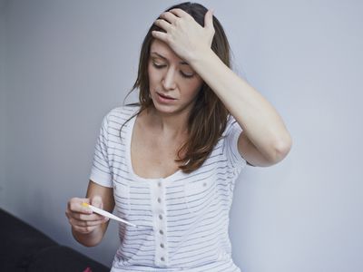 woman taking her temperature and feeling forehead
