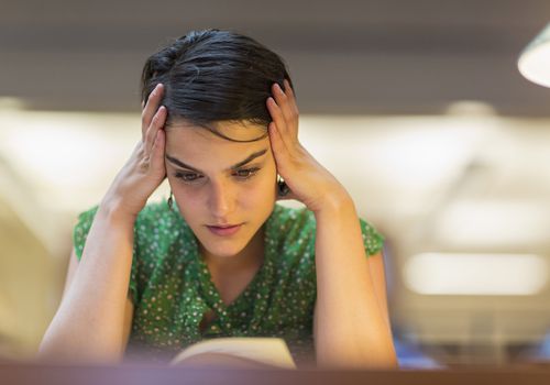 Female student with hands on her head studying in library