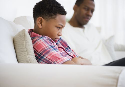 Upset young boy sitting next to his father