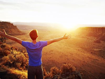 Man standing with arms outstretched looking out at desert canyon at sunset