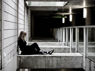 一位沮丧的年轻女子独自坐在一根混凝土柱子旁。丹麦