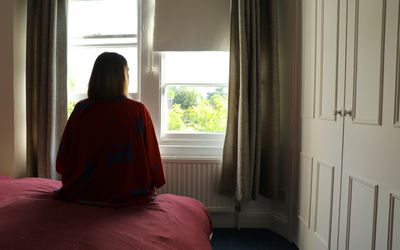 妇女佩带的褐红的长袍，坐桃红色板料凝视外面入窗口暴露树