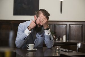 Tired man in suit covering eyes with hand