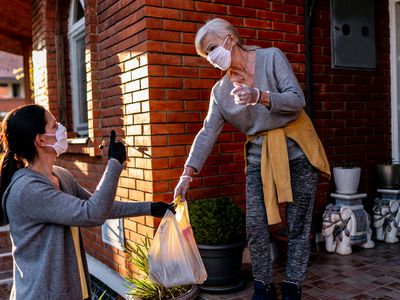 Female volunteer bringing groceries to a senior woman at home under quarantine because of coronavirus.