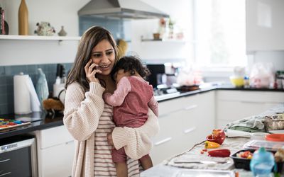 站立在厨房里的妇女，拿着孩子和谈话在电话