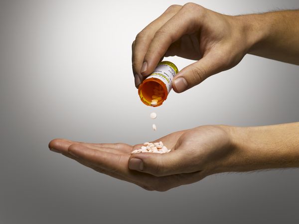 One hand holding a prescription pill bottle and pouring it into the other hand