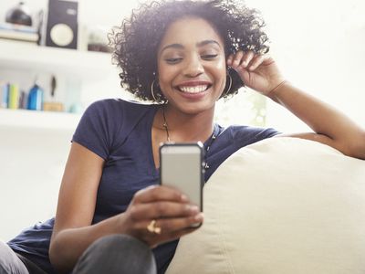 发短信与手机的微笑的非裔美国人的妇女在客厅沙发